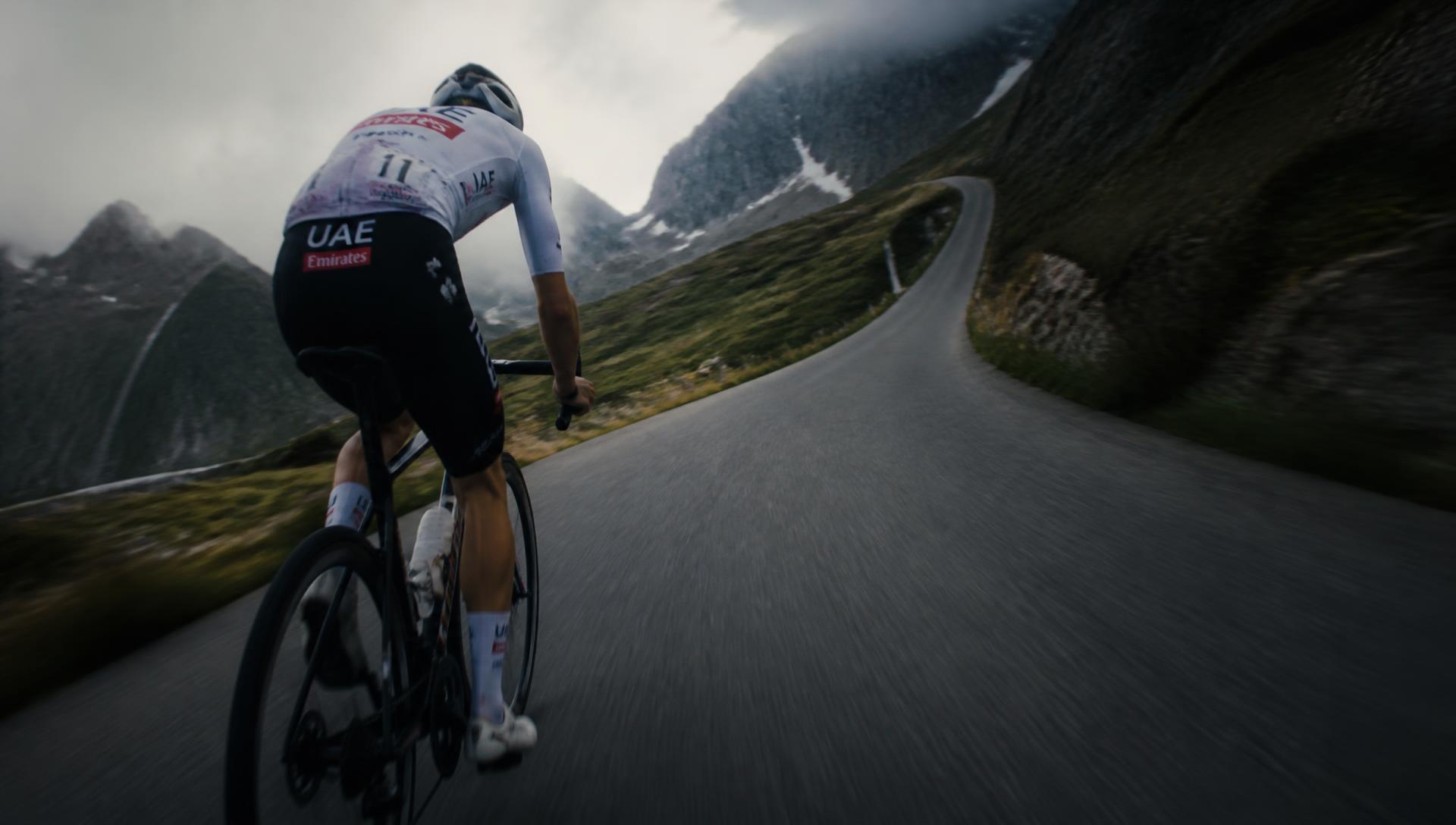 Professional cyclist sprinting up Alpe d'Huez switchbacks at golden hour — FrameYourRide custom route poster hero